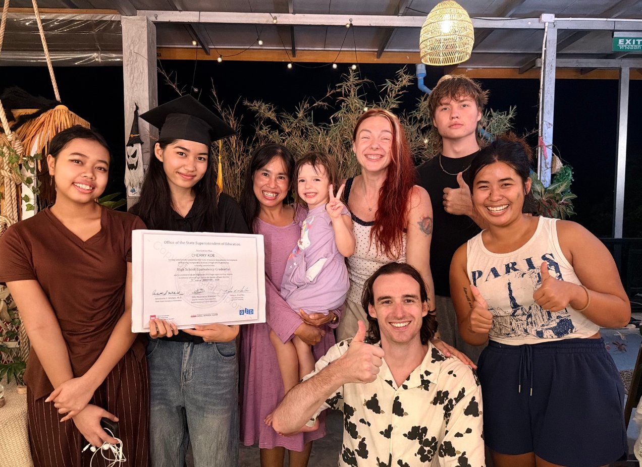 Cherry Koe in a graduation cap holding her GED certificate with friends and volunteers at Wonderland on Koh Tao
