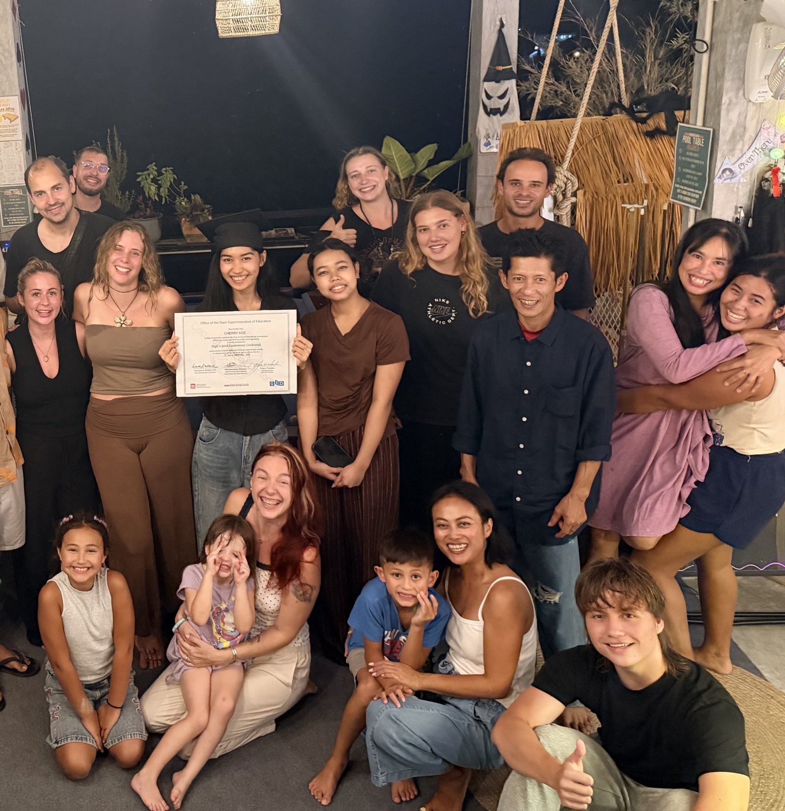 Cherry Koe holds up her GED certificate, surrounded by friends, volunteers and the Wonderland family on Koh Tao