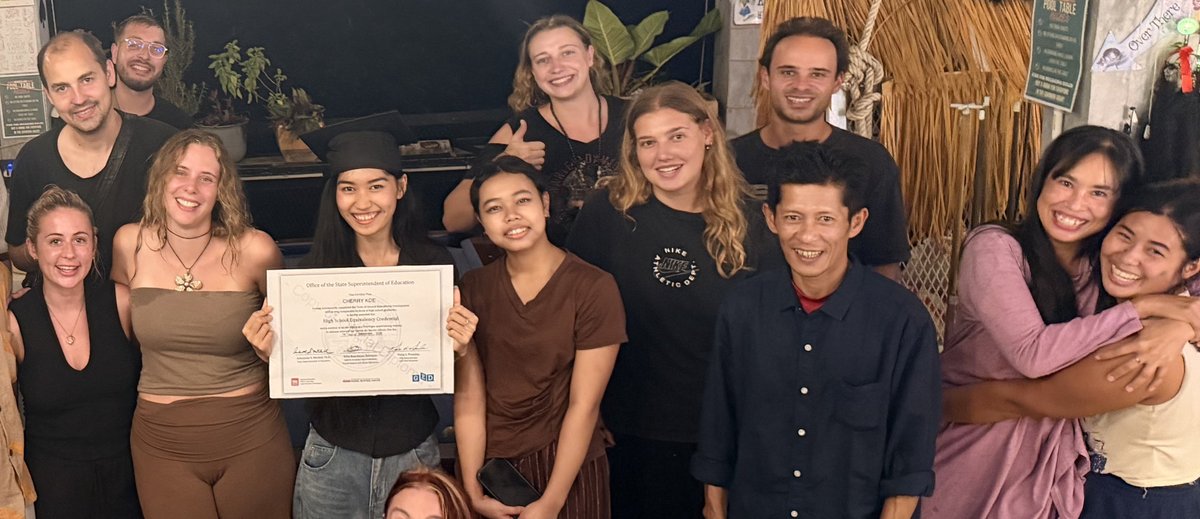 Home 1 Cherry Koe holds up her GED certificate among friends and volunteers on Koh Tao